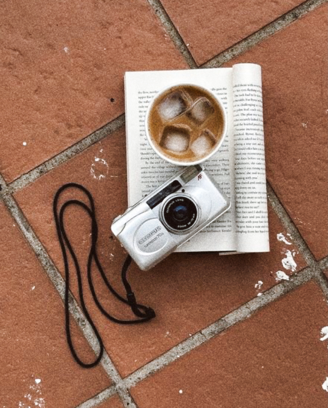Film camera, iced coffee and open book on terracotta tiles